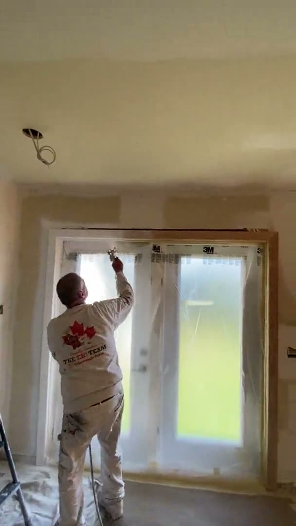 Painter spraying white finish on French-door trim with glass masked in Houston, TX